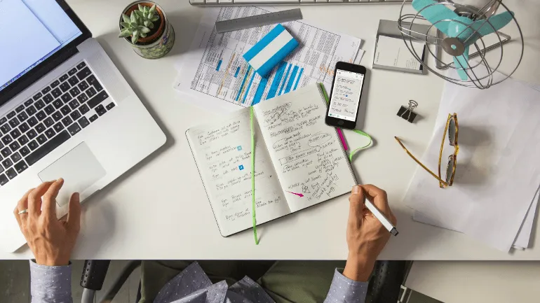Desk workspace with notebook, laptop and phone notes